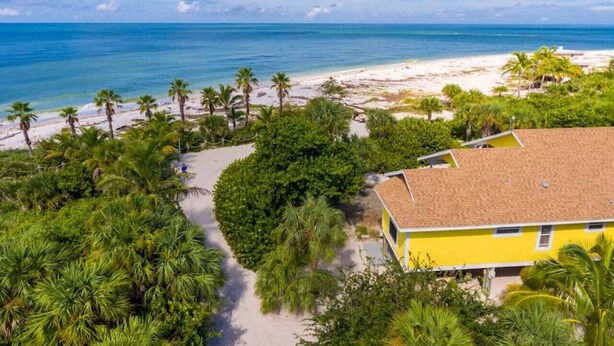 A yellow building with a tiled roof, surrounded by a pathway, palm trees, and a beach. - 3BR Beachfront North Captiva Home with Gulf Views (North Captiva)