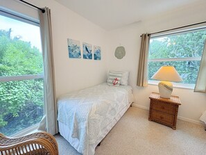 A bedroom with a bed, a nightstand with a lamp, a window with curtains, and wall art.
