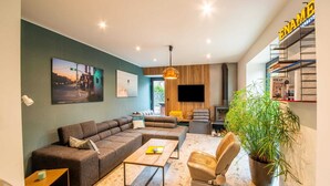 A modern living room with a sectional sofa, a coffee table, a TV, a fireplace, and a bookshelf. - Charming Holiday Home Near Namur With Private Sauna (Jemeppe-sur-Sambre)