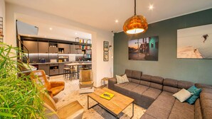 A modern living room with a large sectional sofa, a coffee table, and a dining area with a kitchen in the background. - Charming Holiday Home Near Namur With Private Sauna (Jemeppe-sur-Sambre)