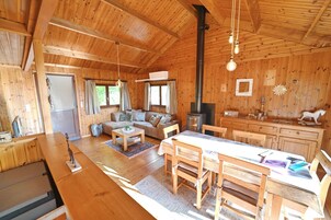 A wooden cabin interior with a dining area, sofa, and kitchen.