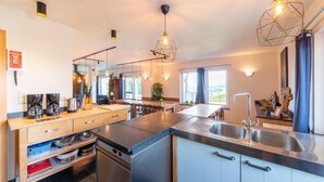 Une cuisine moderne dotée d’un îlot central, d’appareils électroménagers en acier inoxydable et de luminaires suspendus.