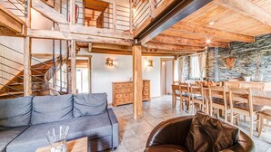 Ein geräumiger Wohnbereich mit einer Holztreppe, einem Esstisch mit Stühlen, einer Couch und einem Ledersessel.