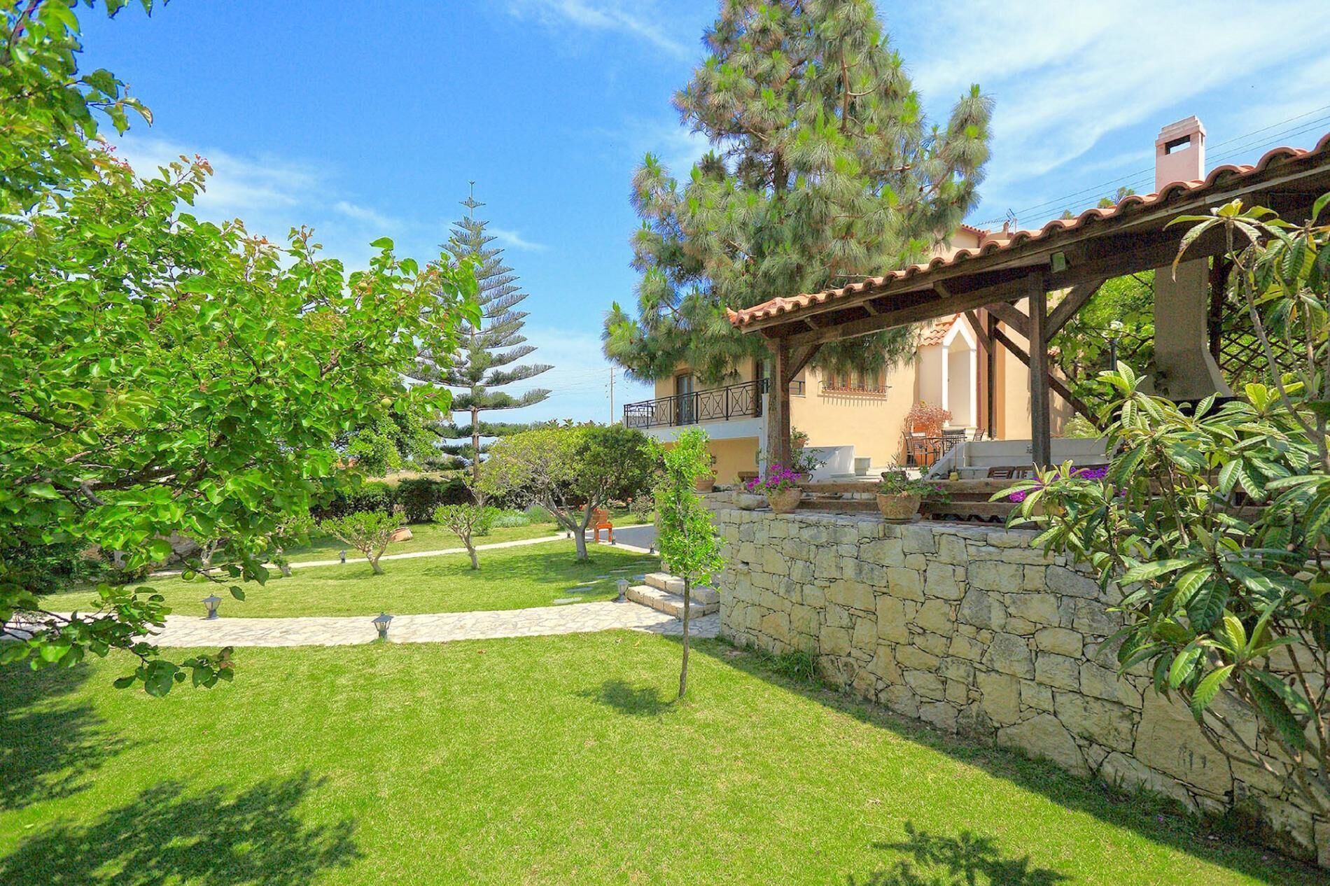 A well-maintained garden with a stone wall, a pergola, and a patio area with outdoor furniture.