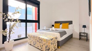 Ein Schlafzimmer mit einem Bett, einem Nachttisch, einer Zimmerpflanze und einem großen Fenster.