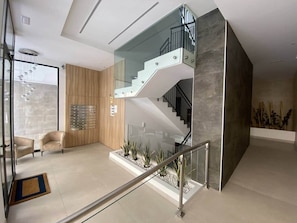A modern interior with a glass staircase, a wooden panel wall, and a seating area with chairs.