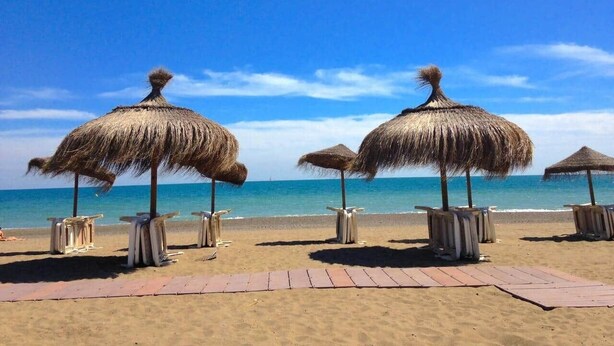 Ein Strand mit Strohdächern und Holzstühlen.