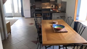 A modern kitchen with grey cabinets, a wooden dining table, and a view of the living area. - Les Vieilles Ombres - Pineau (Bagnizeau)