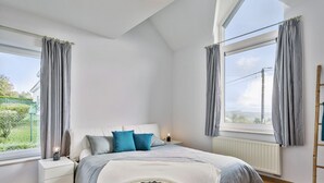A bedroom with a bed, nightstand, and window with curtains. - Pleasant Holiday Home With Recreation Room (Bouillon)