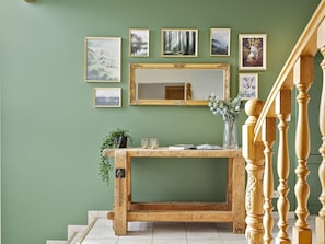 A wooden console table with a mirror and framed pictures on a green wall.