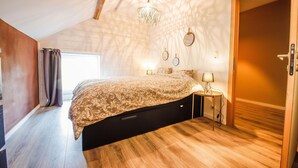 A bedroom with a bed, bedside tables, a chandelier, and a door. - Quietly Located Farmhouse L'echappee Belle (Manhay)