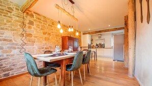 A dining area with a stone wall, wooden beams, and a wooden table with chairs. - Quietly Located Farmhouse L'echappee Belle (Manhay)