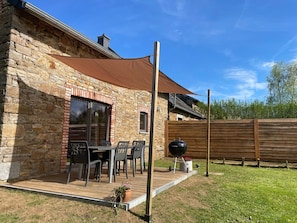 Ein Steinhhaus mit Terrasse, Sitzgelegenheiten im Freien und einem Grill.