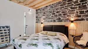 A bedroom with a bed, a wooden headboard, a stone wall, a wooden door, and a chair. - Holiday Home in Biron With Barrel Sauna (Erezee)