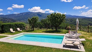 A rectangular swimming pool with a stone border, surrounded by grass and trees, with a mountain view in the background. - Country house with great views, pool, garden,  panoramic terraces, free wifi
 (Torri)