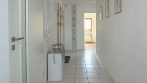 A hallway with a white door, a small white cabinet with a plant, and a tiled floor.
