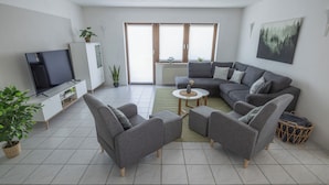 A modern living room with a grey sofa, two armchairs, a coffee table, a TV, and a radiator.