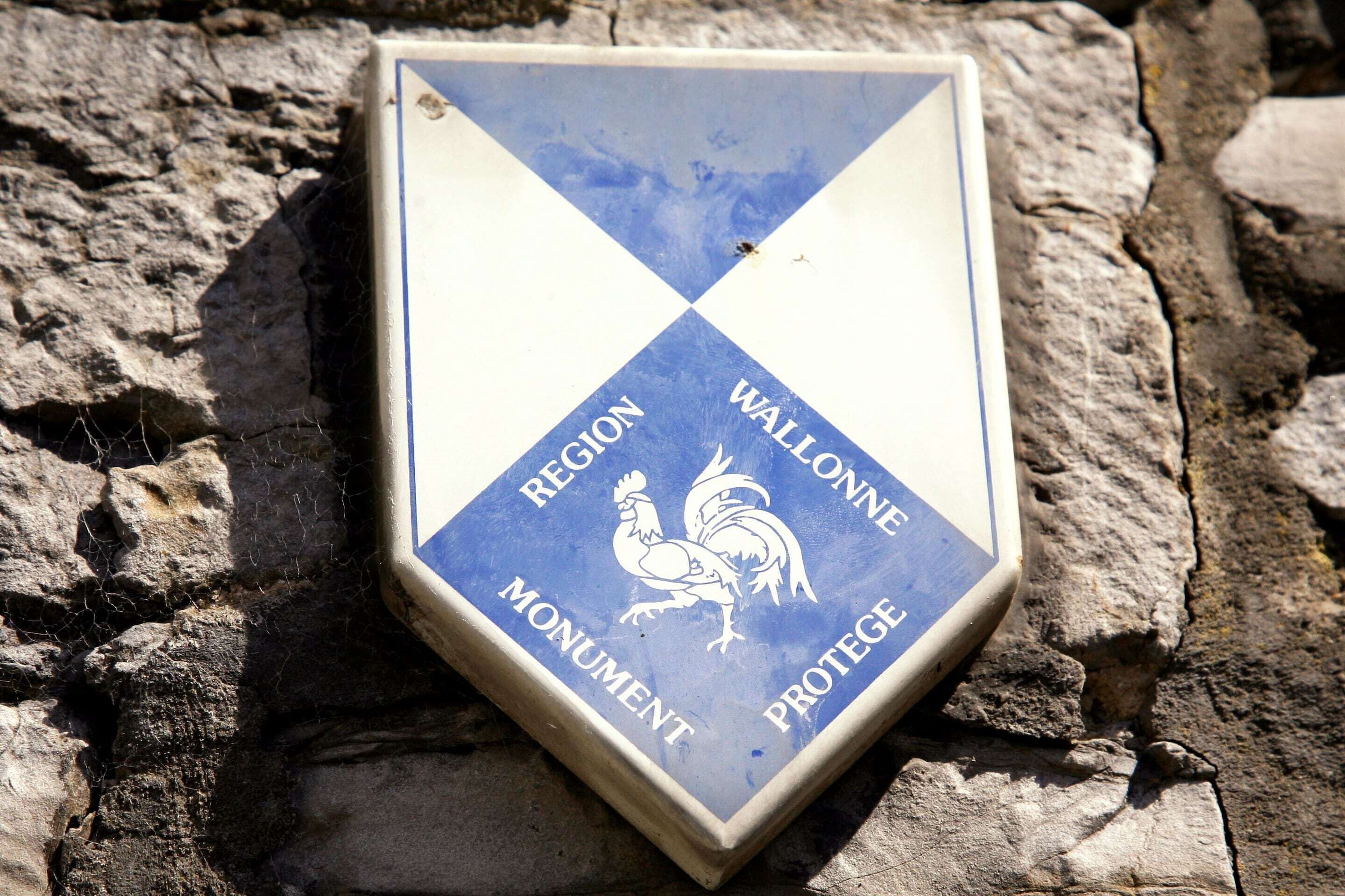 A shield-shaped plaque with a rooster emblem and text reading "REGION WALLONNE MONUMENT PROTEGE".