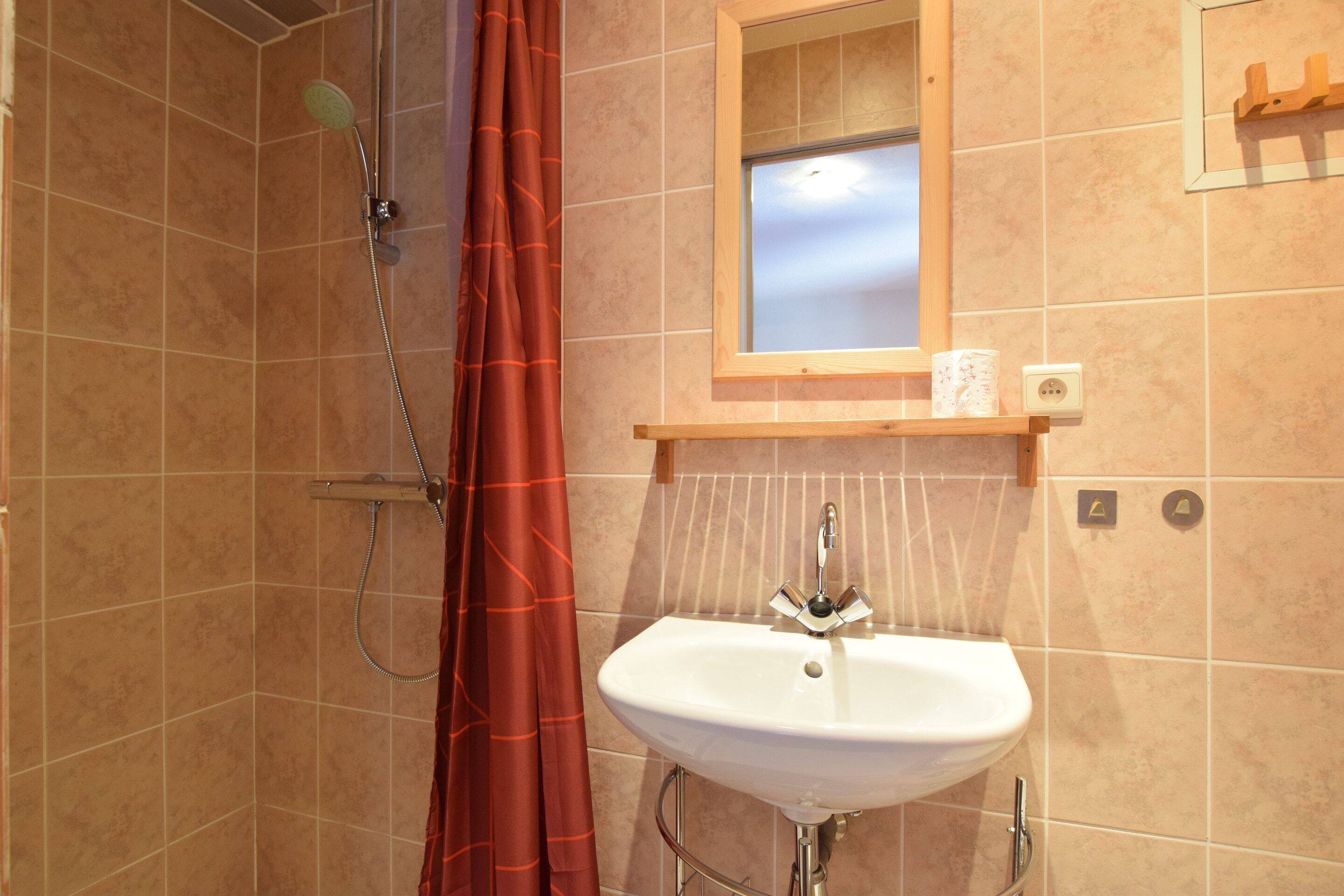 A bathroom with a shower, a sink, and a window above the mirror.
