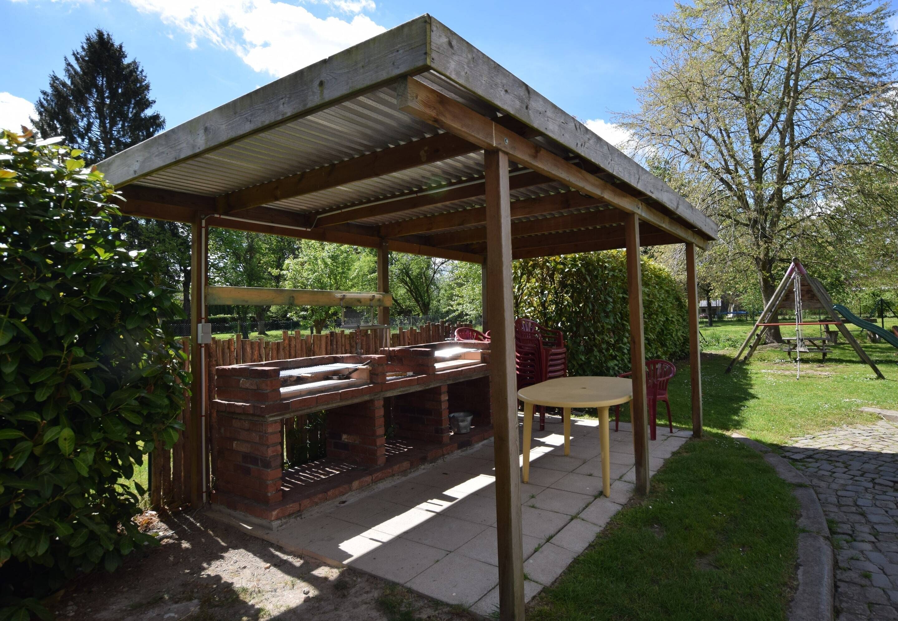 Et overdækket grillområde med en murstensgrill, siddepladser og et bord.