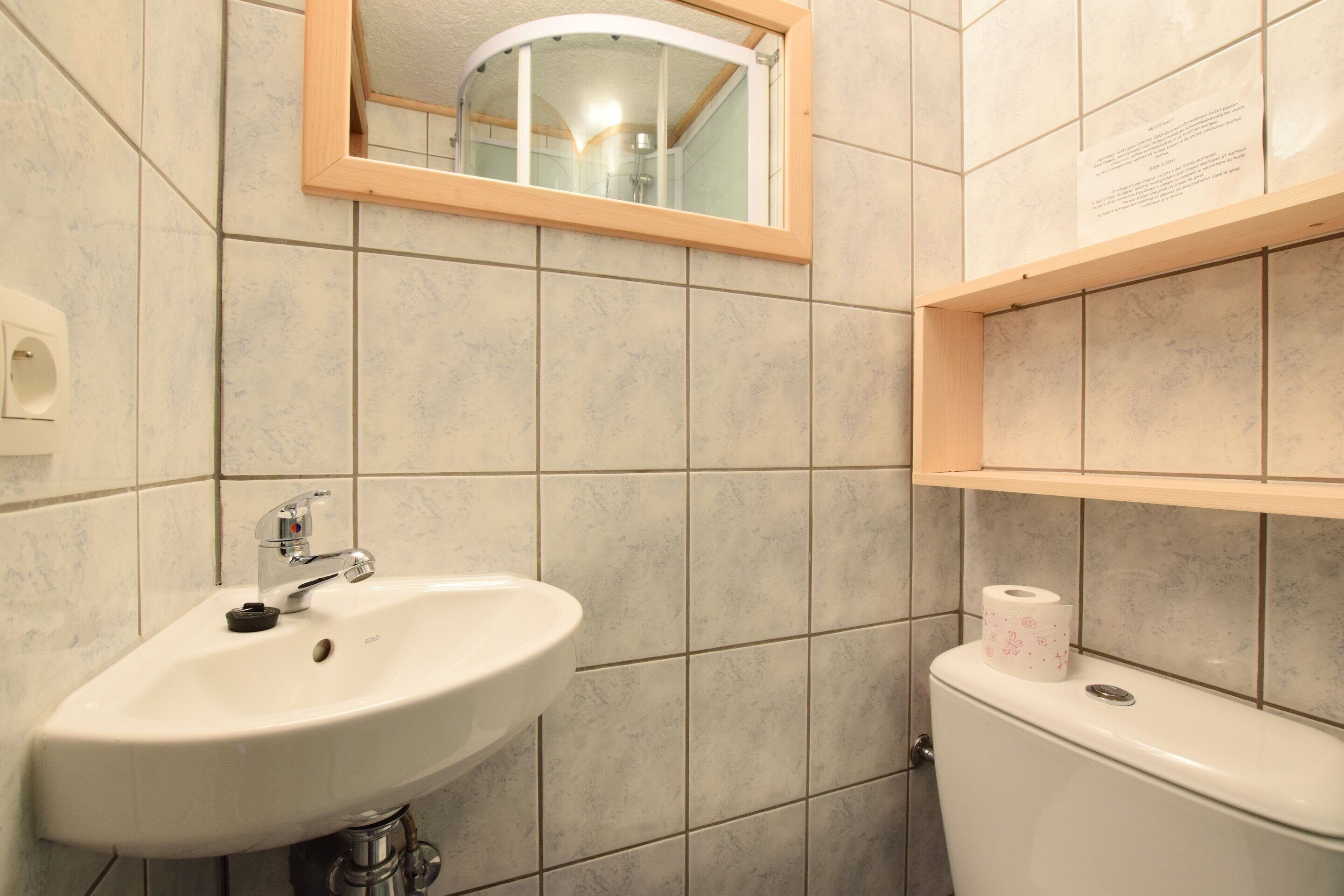 Une salle de bain avec un lavabo blanc, un miroir et des toilettes dotées d’un porte-serviettes en papier.
