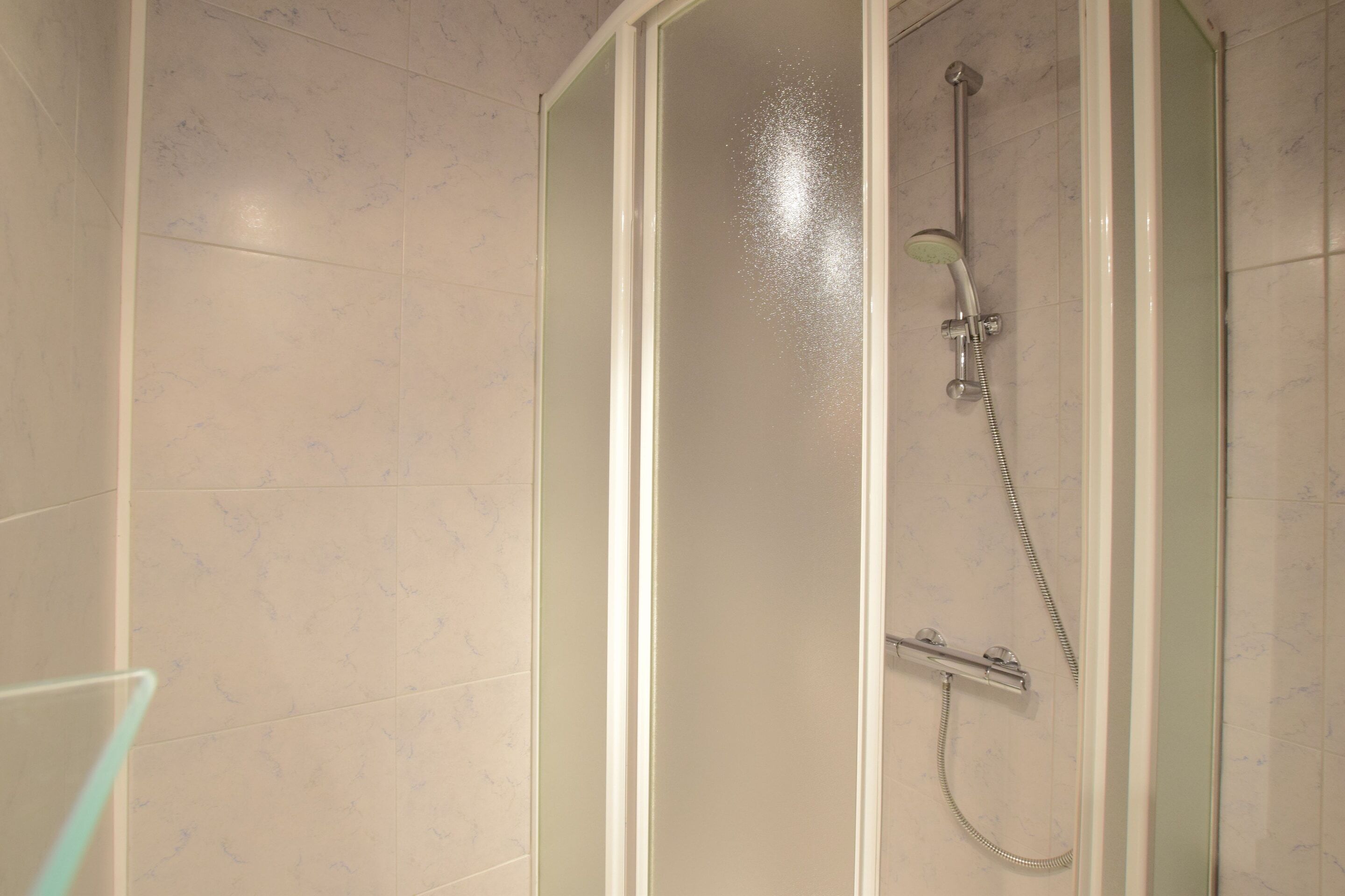 A shower with a glass door, a handheld showerhead, and a handheld shower attachment.