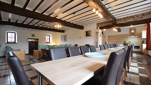 Un espace repas avec une longue table en bois, des chaises noires et un sol à carreaux.