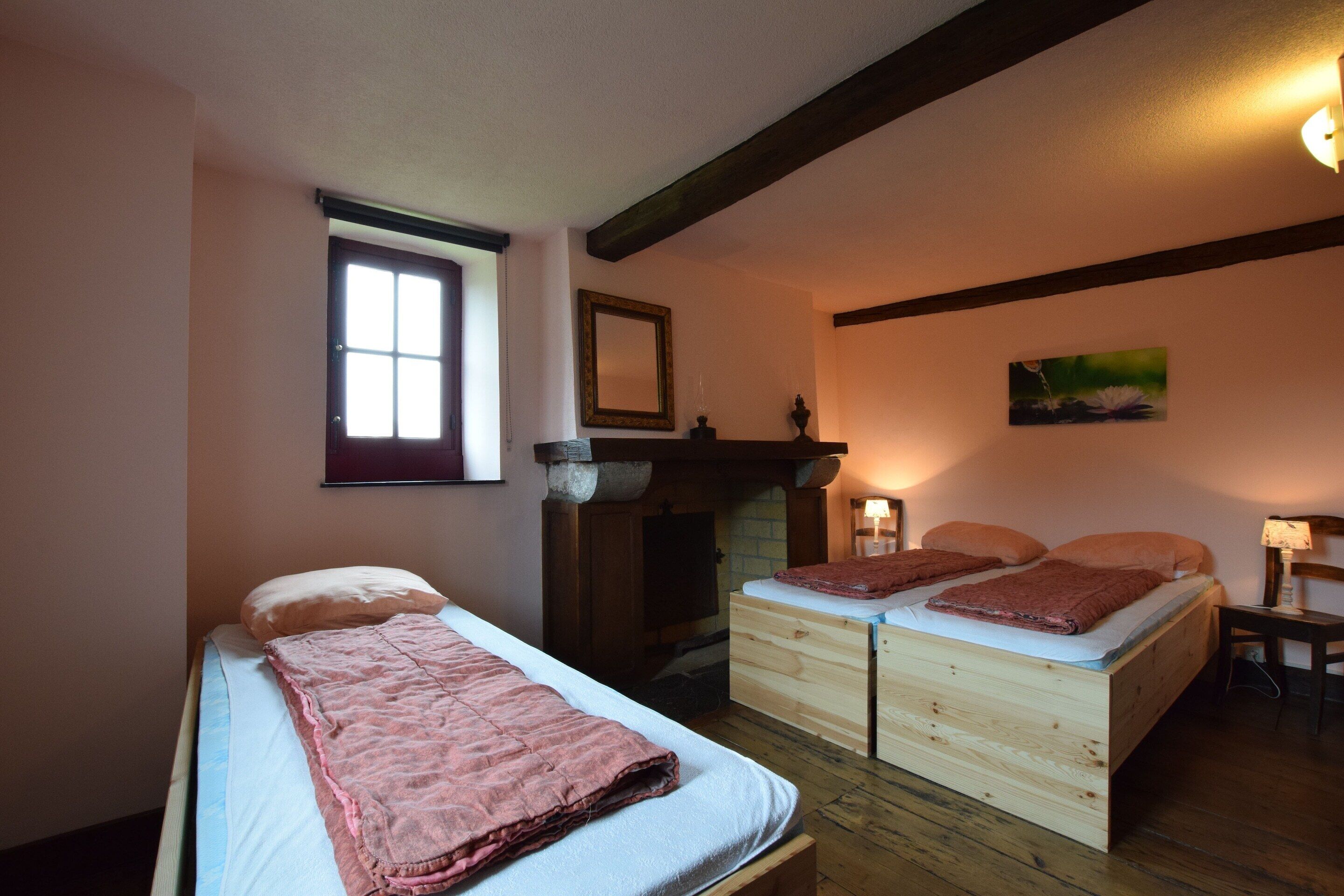 A room with two beds, a fireplace, and a window.