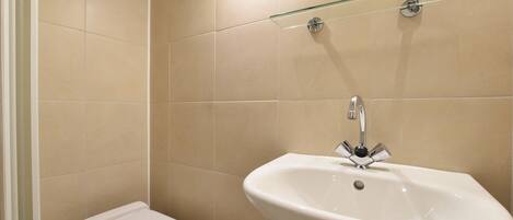 A bathroom with a toilet, a sink, and a glass shelf above the sink.