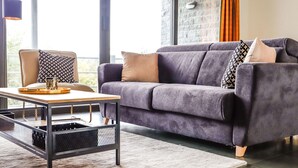 Un saló modern amb un sofà gris, una poltrona estampada, una taula baixa i una finestra gran amb cortines.