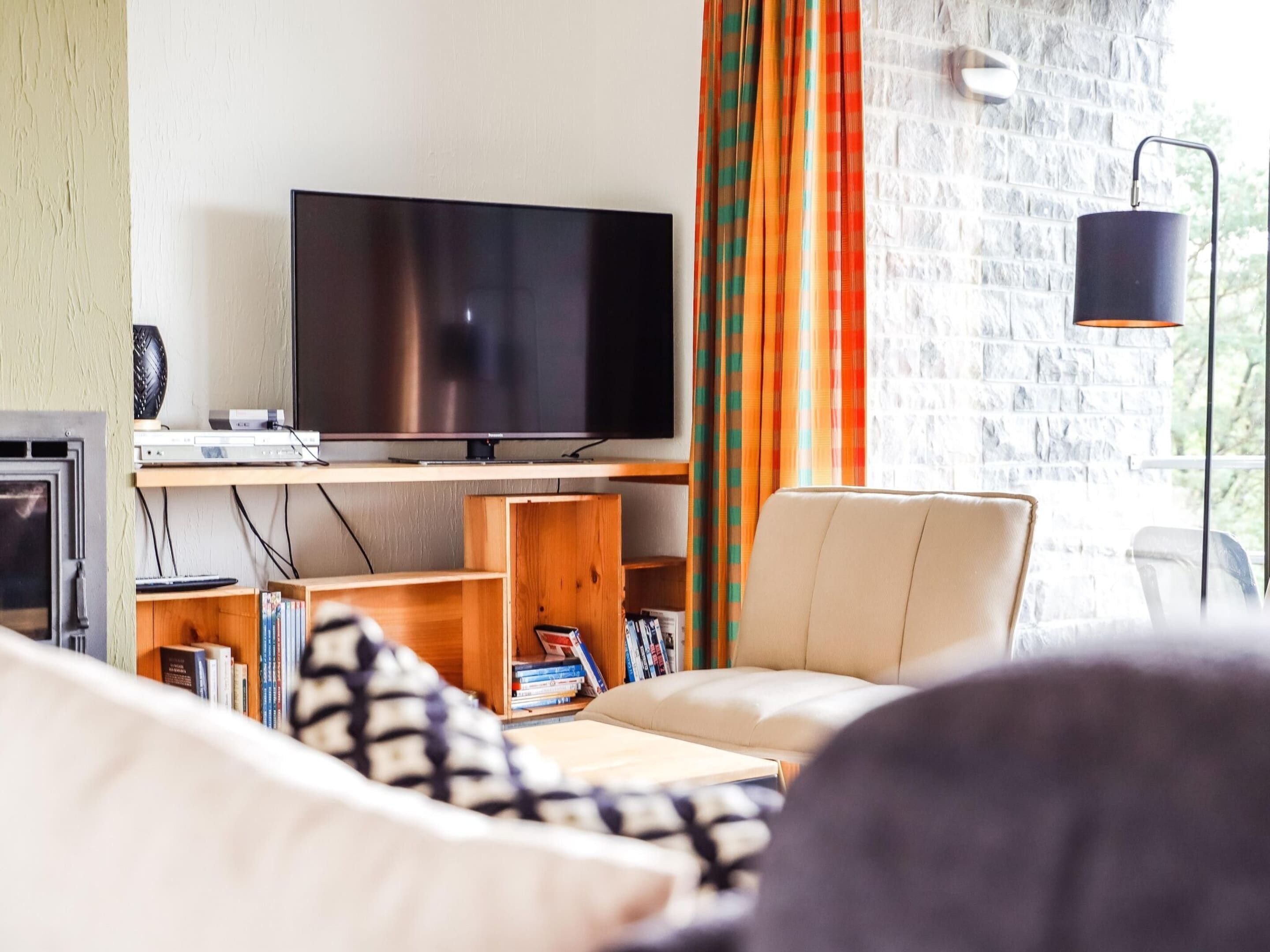 Een woonkamer met een flatscreen televisie op een houten standaard, een bank, een boekenkast en een metselwerk muur.