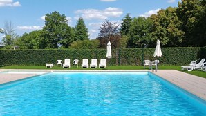 Una piscina rectangular amb aigua blava i cristal·lina, envoltada de gandules i ombrelles blanques.