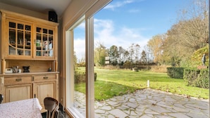 A kitchen with wooden cabinets and a large window overlooking a stone patio. - Holiday Home Het Zuidgoed With Garden (Zedelgem)