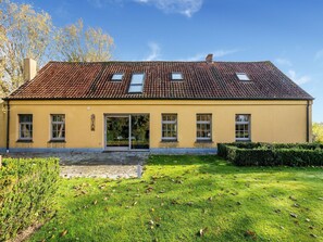 Ein gelbes Gebäude mit einem Ziegeldach, zahlreichen Fenstern und einem gepflasterten Eingangsbereich.
