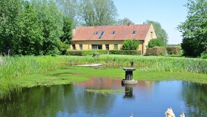 A house with a red-tiled roof, surrounded by a pond and lush greenery. - Holiday Home Het Zuidgoed With Garden (Zedelgem)