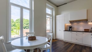 A modern kitchen with white cabinetry, a round dining table, and large windows offering a view of greenery.