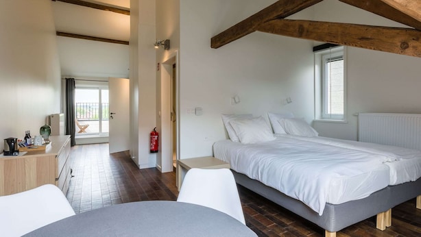 A bedroom with a bed, bedside tables, a desk, and a chair. There is a window with blinds and a radiator.