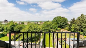 A balcony with a view of a green landscape, including trees and a distant village.