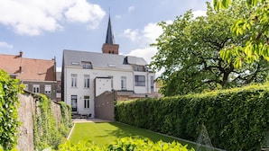 A modern two-story house with a garden and a church steeple in the background.