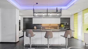 Una cocina moderna con una isla central, tres taburetes de bar y una zona de estar integrada.