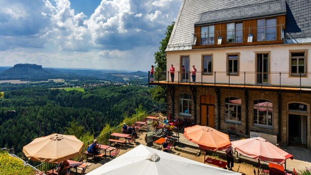 A hotel with outdoor seating, a balcony, and a view of a forested valley. - Great Holiday Home With Terrace Near Saxon (Hohnstein)