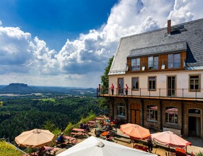 A hotel with outdoor seating, a balcony, and a view of a forested valley. - Great Holiday Home With Terrace Near Saxon (Hohnstein)