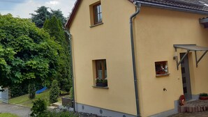 A two-story house with a yellow exterior, a tiled roof, and a small porch area with potted plants. - Great Holiday Home With Terrace Near Saxon (Hohnstein)