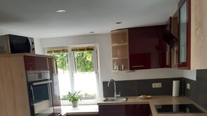 A modern kitchen with dark cabinetry, a built-in oven, a sink, and a window with a view of greenery. - Great Holiday Home With Terrace Near Saxon (Hohnstein)