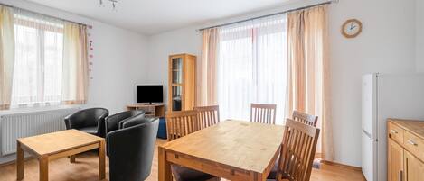 A spacious living area with a wooden dining table, comfortable seating, a television, and a refrigerator.