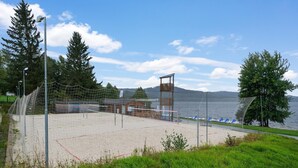 Una cancha de voleibol de playa con red, una torre de salvavidas y vista a un lago.