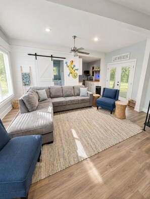 A modern living room with a sectional sofa, a blue armchair, a woven rug, and a ceiling fan.