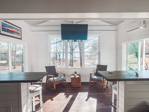 A room with a large window, two chairs, a small table, and a TV mounted on the wall.