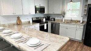 A modern kitchen with white cabinets, a large island with bar stools, stainless steel appliances, and pendant lighting. - Lake Murray Cottage w/ Private Dock, Fire Pit & Kayaks - Near Martin's Landing (Prosperity)