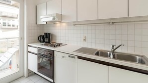 Moderni keittiö, jossa on valkoiset kaapit, sisäänrakennettu uuni, astianpesukone ja ruostumattomasta teräksestä valmistettu pesuallas.